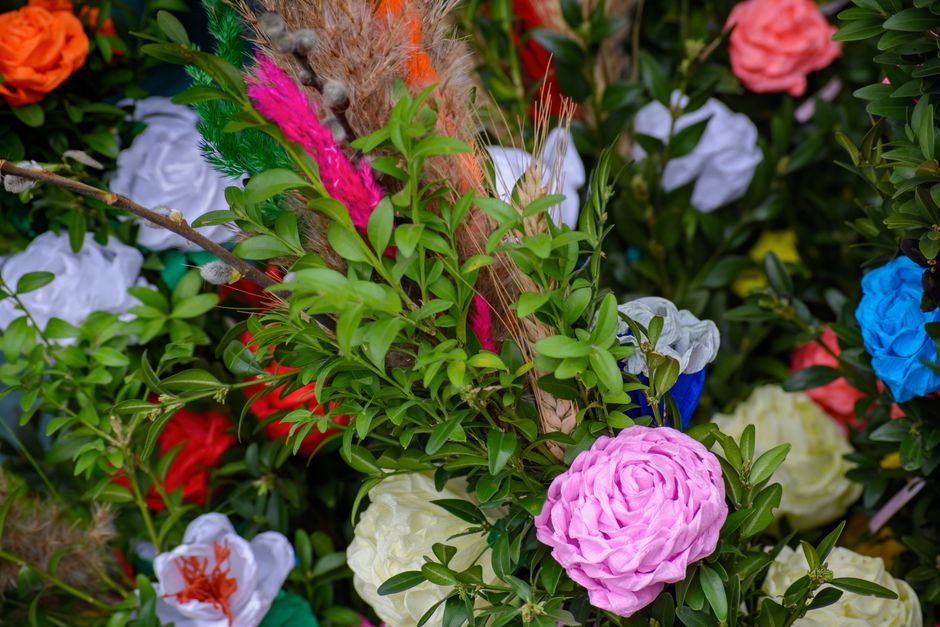 A vibrant floral arrangement featuring a variety of fresh flowers, including a large pink rose-like bloom and smaller white, red, orange, blue, and yellow blossoms, all surrounded by lush green foliag