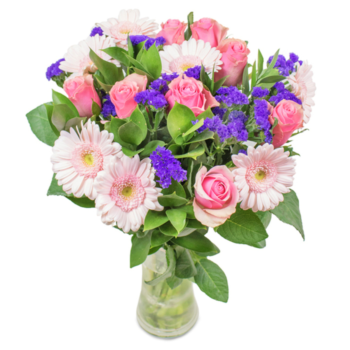A vibrant floral arrangement is presented in a crystal-clear glass vase, set against a bright backdrop evocative of Becontree Heath's welcoming streets. The focal point features a blend of seven to nine classic pink roses, their petals playfully unfurling from tight buds into generous spirals. Alongside, five to seven pale pink gerbera daisies bask under soft natural light, their oversized blooms and creamy centers radiating gentle elegance. Interwoven within the display, clusters of vivid purple statice add depth and lively energy, creating textural contrast that catches the eye-much like vibrant corners of the local community market. Lush, deep green foliage overflows around the base of the bouquet, enhancing its freshness and giving the arrangement a sense of abundance and vitality. The transparent vase allows stems and water to be clearly seen, highlighting the natural beauty and freshness characteristic of same-day flower delivery throughout Becontree Heath. This elegant mix of pink roses, gerberas, and purple accent flowers is suitable for birthdays, anniversaries, Mother's Day, or as a decorative accent in homes and offices across the area, delivering sentiments of joy, celebration, and lasting affection.